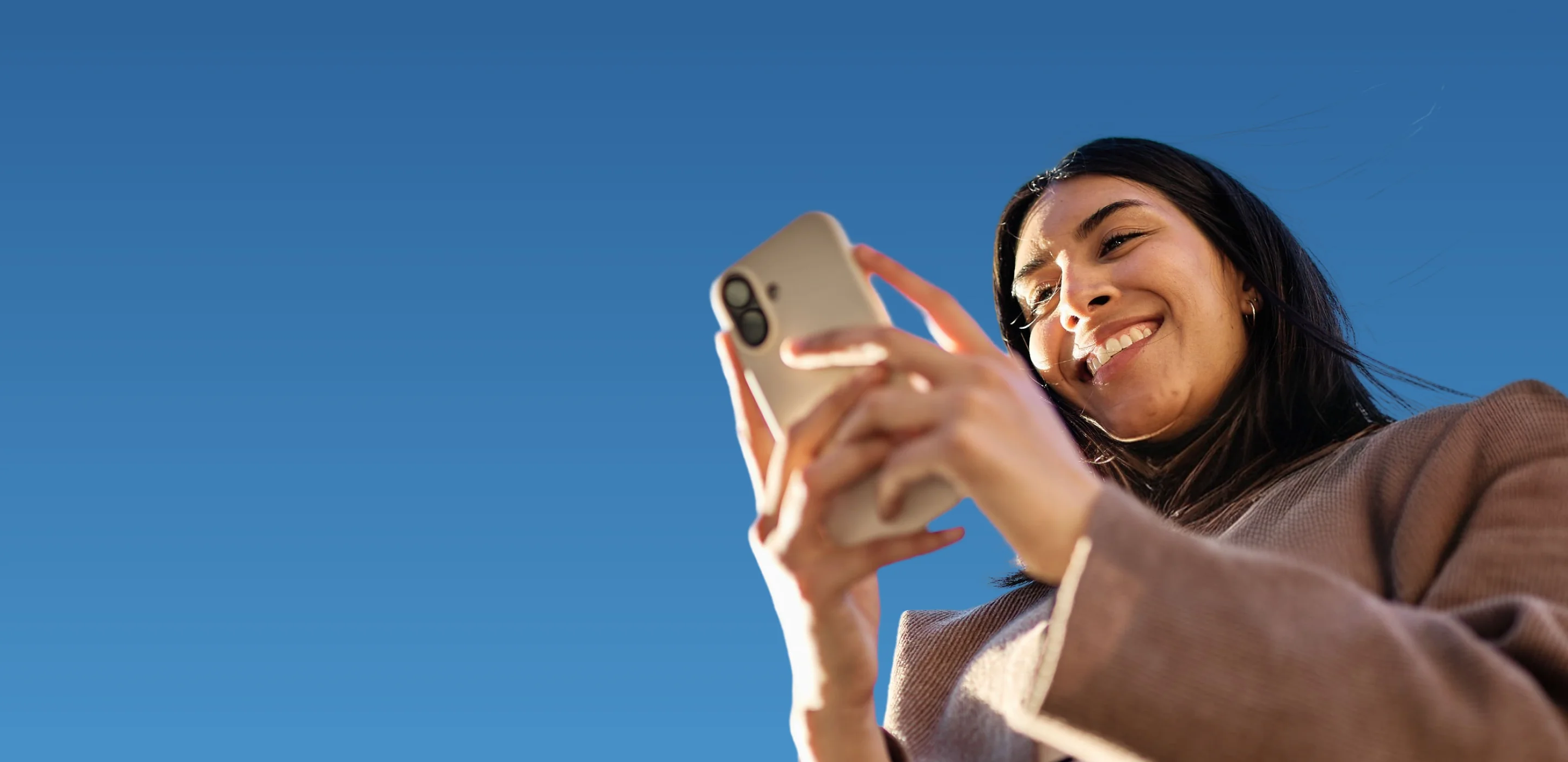 Woman smiling while using her phone against a blue sky