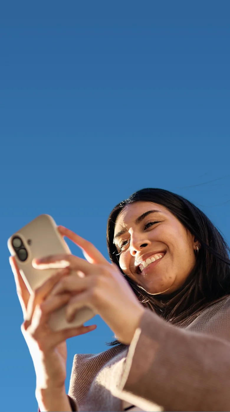 Woman smiling while using her phone against a blue sky